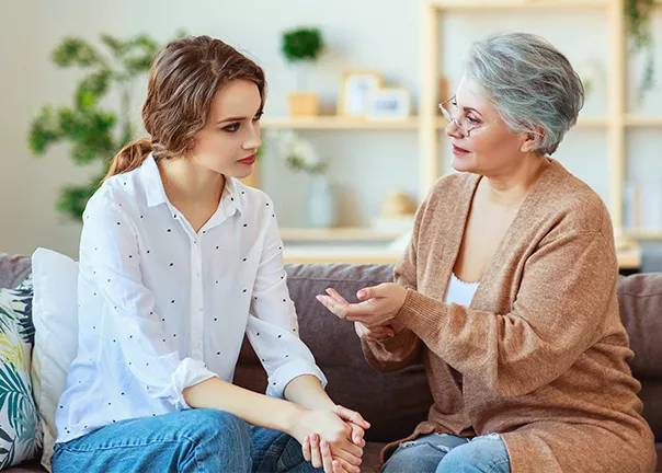 Older mother talking to adult daughter on couch. using hand gestures making eye contact