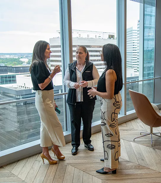 Three female employees talking in the Evolent office near large windows and seating area
