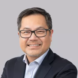 Headshot of Chief Clinical Officer Dr. Von Nguyen. Asian man in dark framed glasses smiling with short black hair, light blue button down top with black suit jacket. 