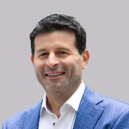 Headshot of Russell Glass. White male with black hair, smiling, white button down collared shirt, blue blazer, with gray background.